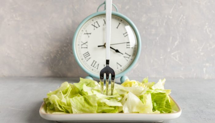 Alarm clock and plate with green iceberg lettuce,  Intermittent fasting concept, ketogenic diet, weight loss